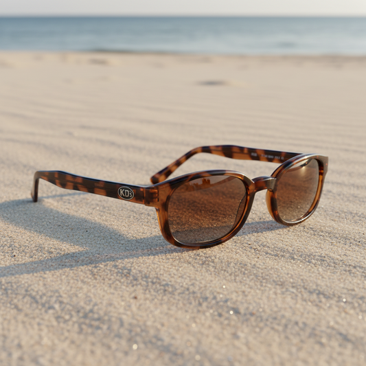 Lunettes de soleil KD's 200 monture écaille brune à verres ambrés, petite taille, photographiées sur un sable clair en bord de mer.